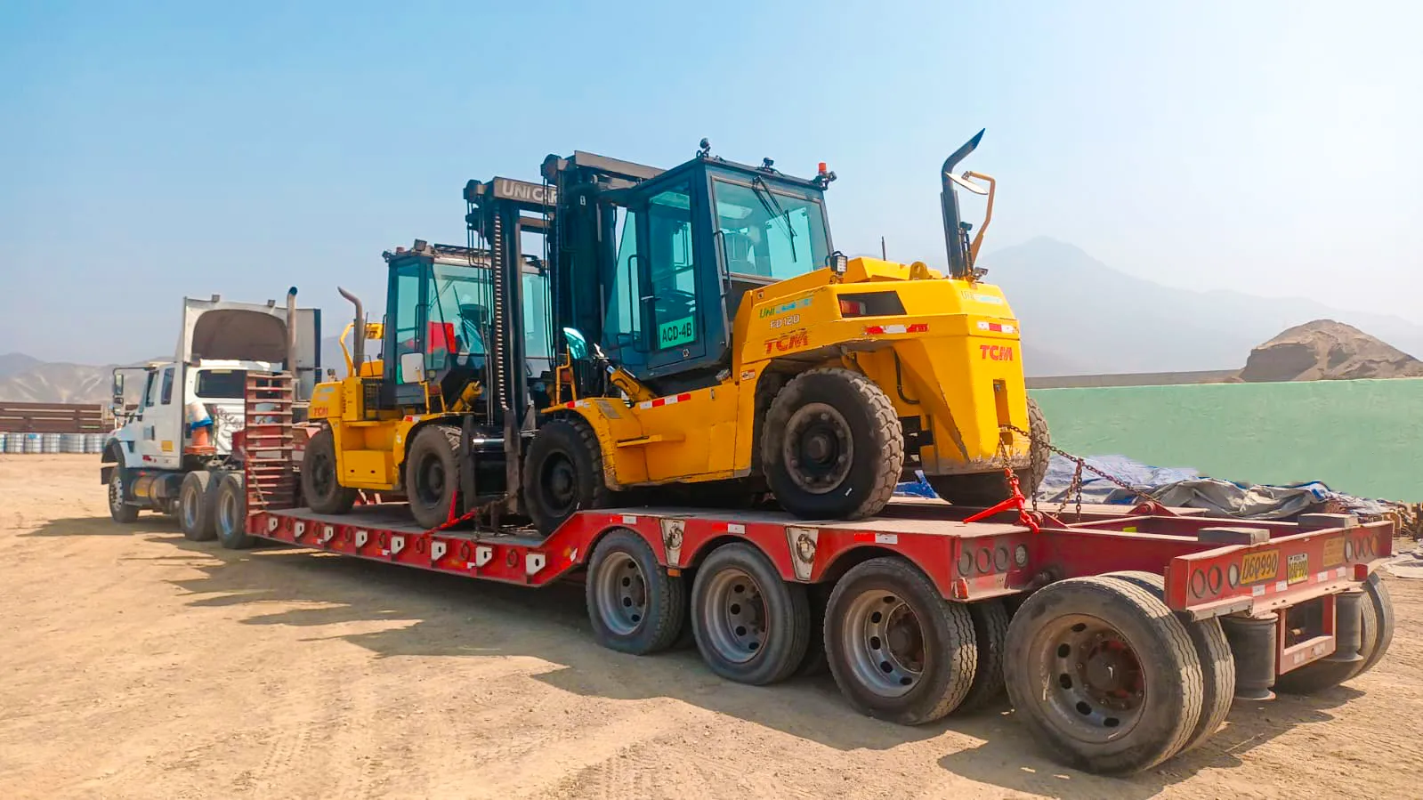 Tracto con cama baja de varios ejes transportando montacargas amarillos